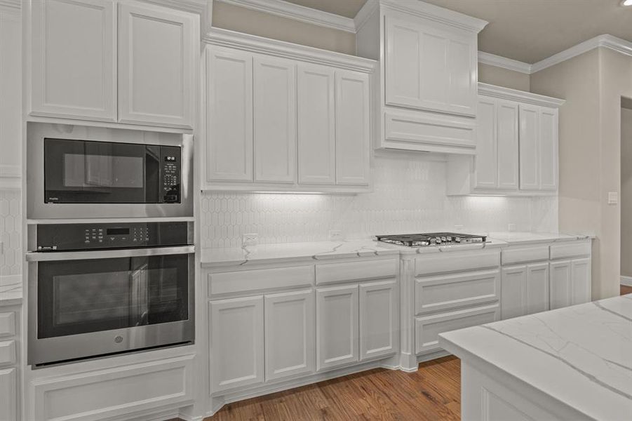 Kitchen featuring white cabinetry, stainless steel appliances, light stone countertops, and crown molding