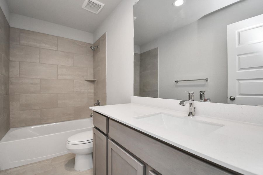 Secondary bath features tile flooring, bath/shower combo with tile surround, light stained wood cabinets, beautiful light countertop. Sample photo of completed home with similar floor plan. Actual colors and selections may vary.