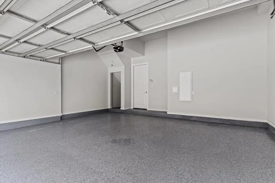 Spacious garage featuring a durable speckled epoxy floor finish, light gray painted walls, and a white interior door