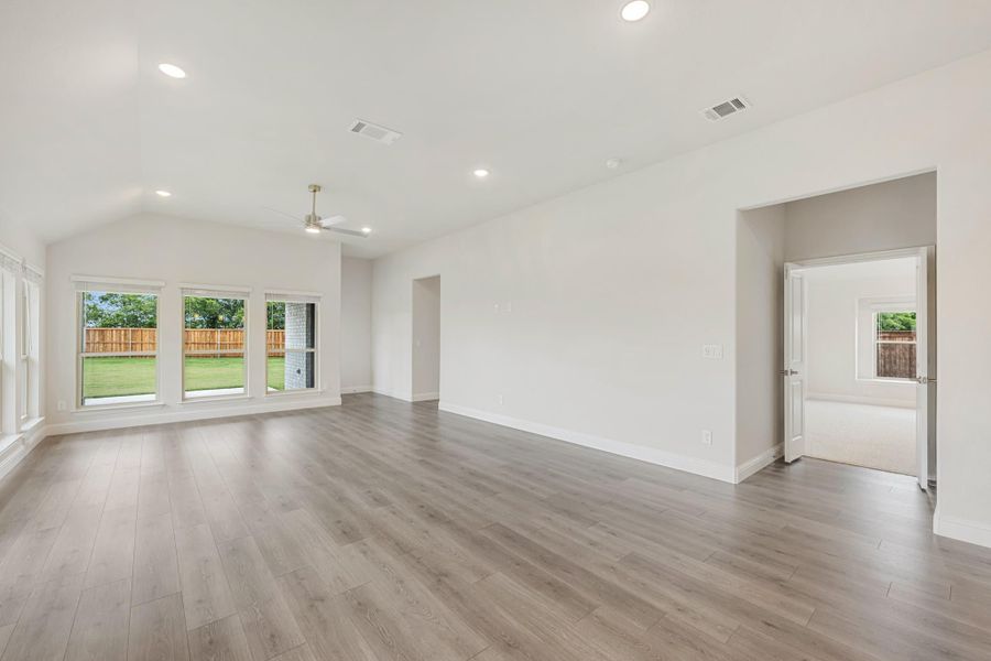 Open living room with vaulted ceiling, ceiling fan, hardwood floors, and large windows overlooking backyard Open living room with vaulted ceiling, ceiling fan, hardwood floors, and large windows overlooking backyard