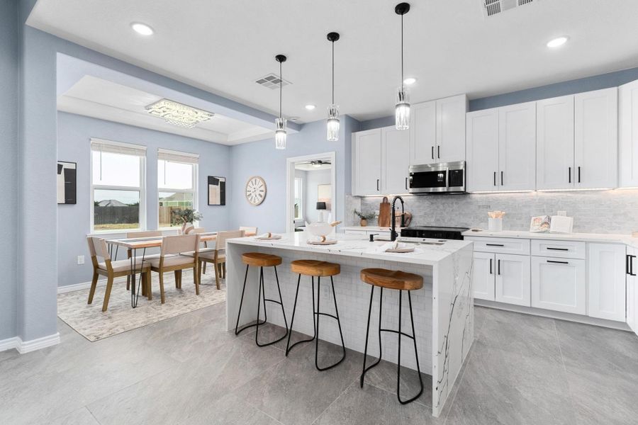 Kitchen featuring tasteful backsplash, stainless steel microwave, white cabinetry, a breakfast bar, and a center island with sink Kitchen featuring tasteful backsplash, stainless steel microwave, white cabinetry, a breakfast bar, and a center island with sink