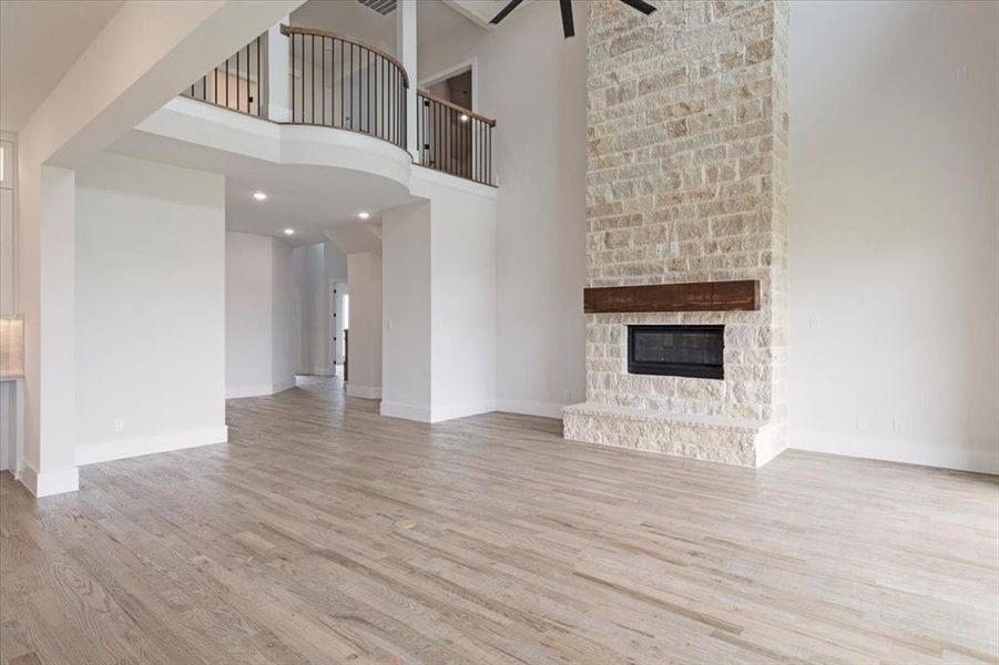 Unfurnished living room with ceiling fan, a towering ceiling, light hardwood / wood-style floors, and a fireplace