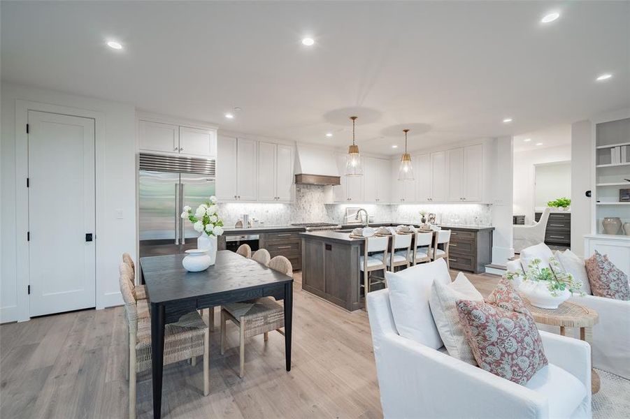 Kitchen with premium range hood, built in fridge, white cabinets, decorative backsplash, and light hardwood / wood-style floors