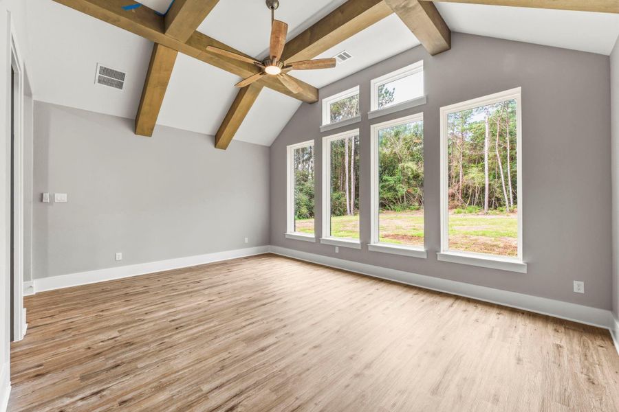 Spacious game room with dramatic wood beams, vaulted ceiling, and expansive windows overlooking the wooded backyard.