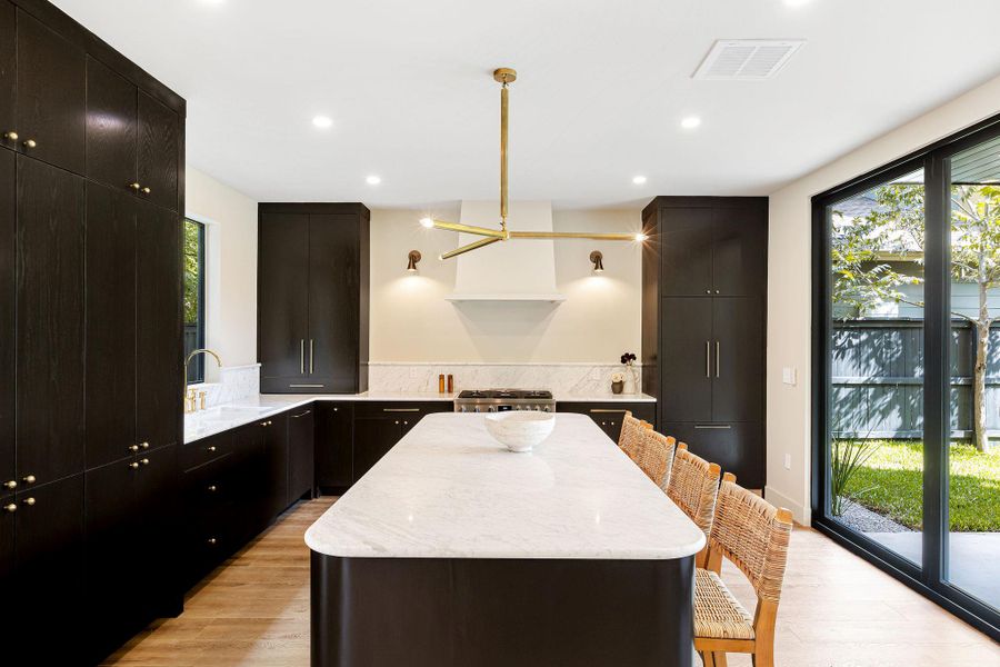 Kitchen with a breakfast bar, light stone counters, dark cabinets, light wood-type flooring, and a center island
