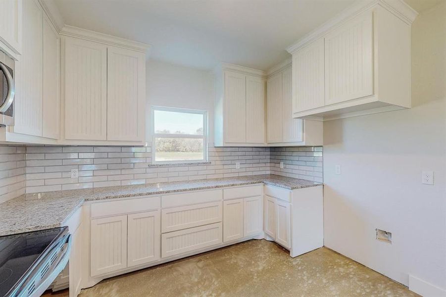 Kitchen with backsplash, white cabinetry, light stone counters, and appliances with stainless steel finishes