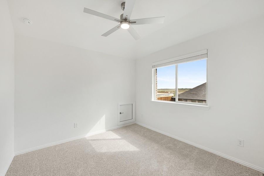 Empty bedroom with white walls, ceiling fan, carpet flooring, and a window with outdoor views