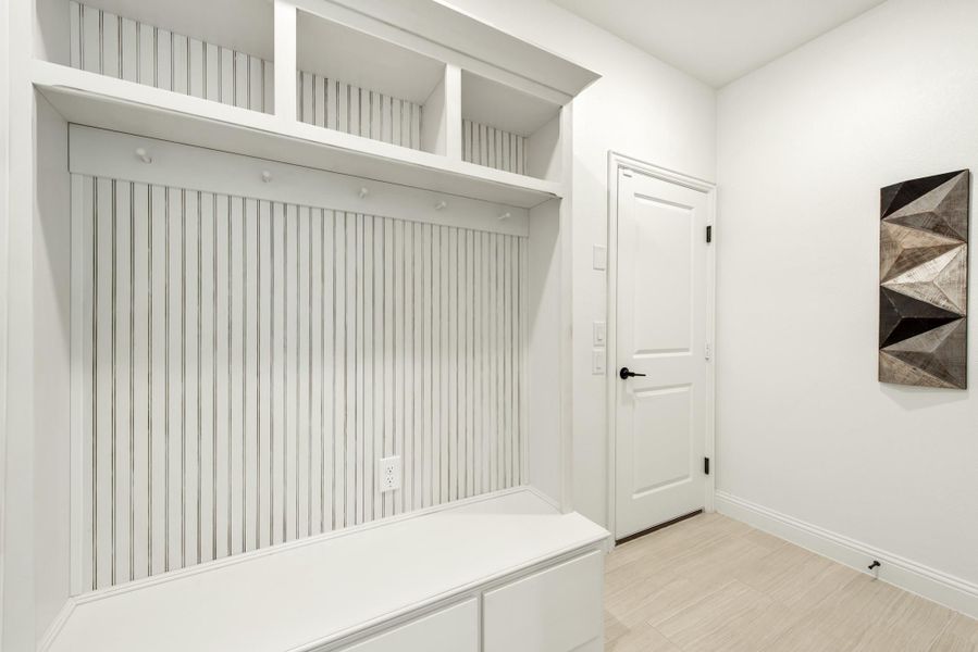 White mudroom with built-in bench, upper shelves, coat hooks, and beadboard paneling on light tile floor