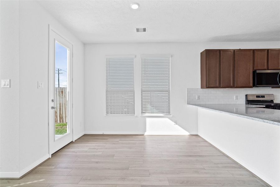 Start your day with a warm cup of coffee and quality time in this charming dining area! Highlights include large windows with blinds, custom neutral paint, vinyl plank flooring, high ceilings, and a convenient door leading to the rear patio and backyard.