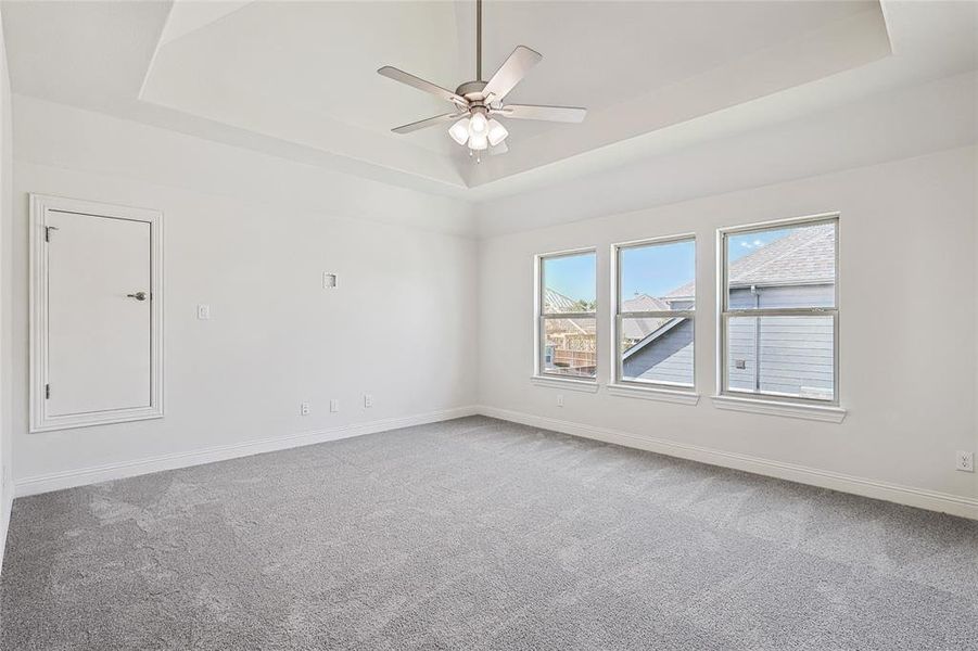 Empty room with carpet floors, ceiling fan, and a raised ceiling