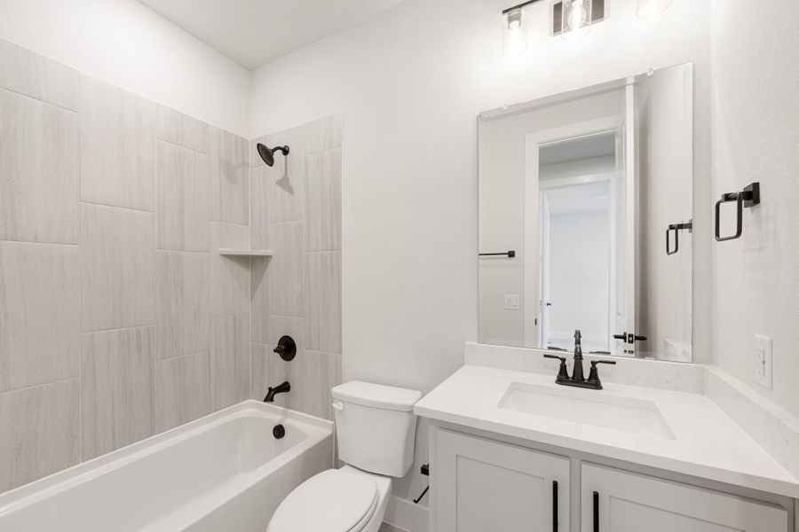 Bathroom with tiled tub-shower combo, white vanity with black fixtures, and wall mirror