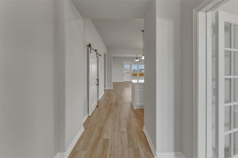 Interior hallway featuring wood-finish flooring, white baseboards, and a barn door with black hardware Interior hallway featuring wood-finish flooring, white baseboards, and a barn door with black hardware
