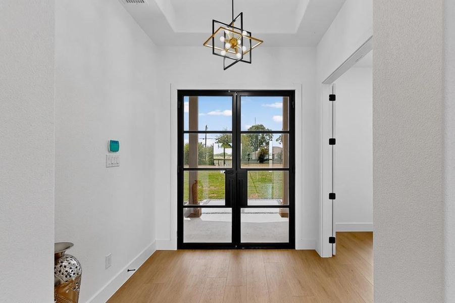 Entryway featuring light wood-style floors, a chandelier, and a tray ceiling