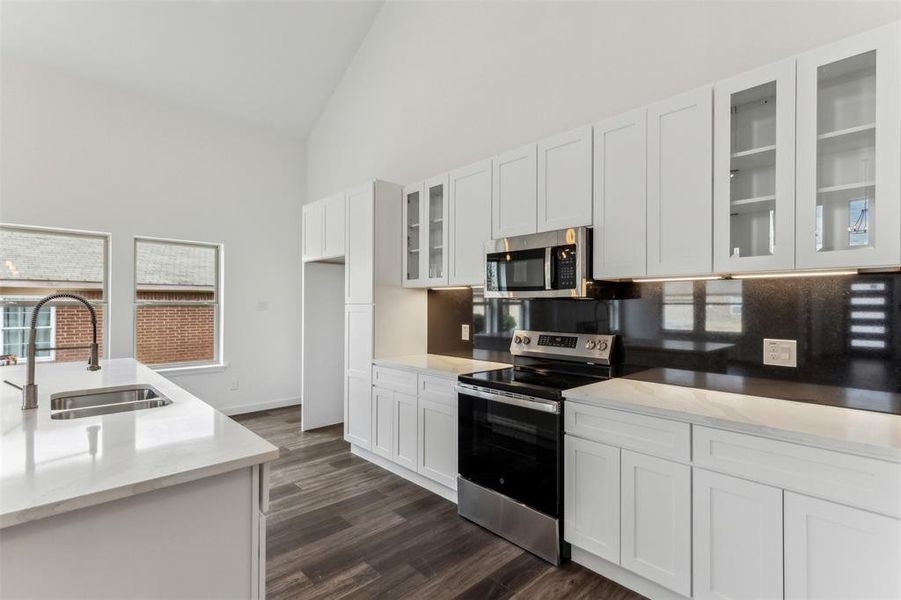 Kitchen featuring appliances with stainless steel finishes, dark hardwood / wood-style floors, high vaulted ceiling, white cabinetry, and sink