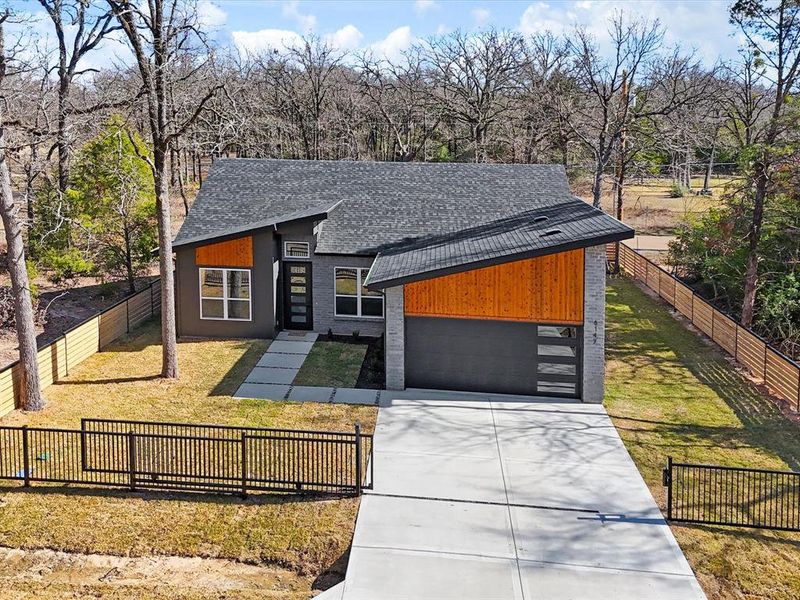 Contemporary home with a shingled roof, concrete driveway, a garage, and view of wooded area