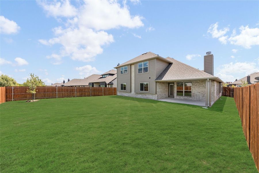 Two-story brick home with covered patio, large fenced backyard, and green lawn