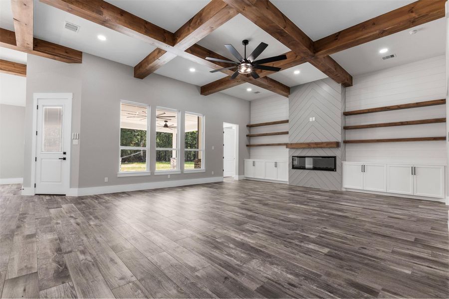 Spacious living area with elegant wood beam ceilings, sleek built-in shelves, and a modern fireplace, complemented by large windows for ample natural light.