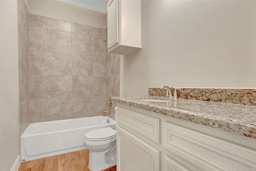 This bathroom features a modern design with a granite countertop, white cabinetry, and a bathtub with tiled surround. The floor is finished with wood-like tiles, offering a clean and elegant look. This bathroom features a modern design with a granite countertop, white cabinetry, and a bathtub with tiled surround. The floor is finished with wood-like tiles, offering a clean and elegant look.