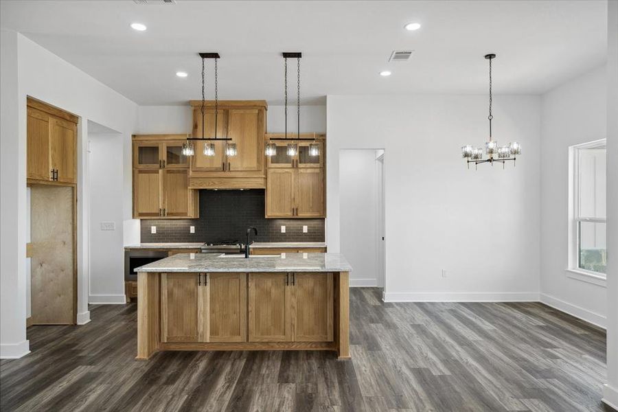 Kitchen featuring dark wood finished floors, backsplash, a center island with sink, a chandelier, and recessed lighting