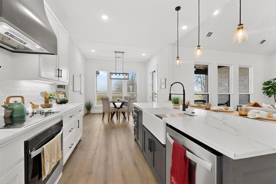 Dual tone kitchen featuring two tone cabinets, extractor fan, decorative light fixtures, stainless steel appliances, and light wood finished floors