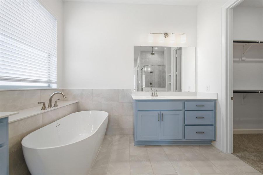 Modern bathroom featuring a freestanding soaking tub, single vanity with light blue cabinetry, white countertop, and brushed nickel fixtures