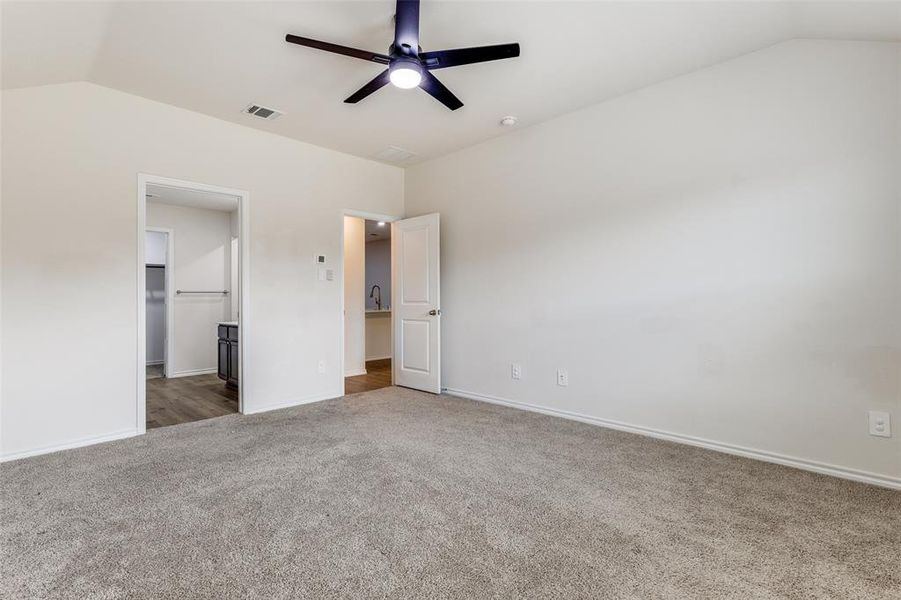 Spacious room featuring vaulted ceilings, neutral-toned carpeting, and a modern ceiling fan Spacious room featuring vaulted ceilings, neutral-toned carpeting, and a modern ceiling fan
