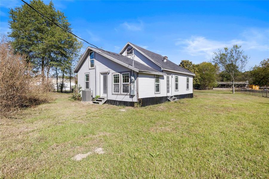 View of side of home with entry steps, a lawn, and a shingled roof