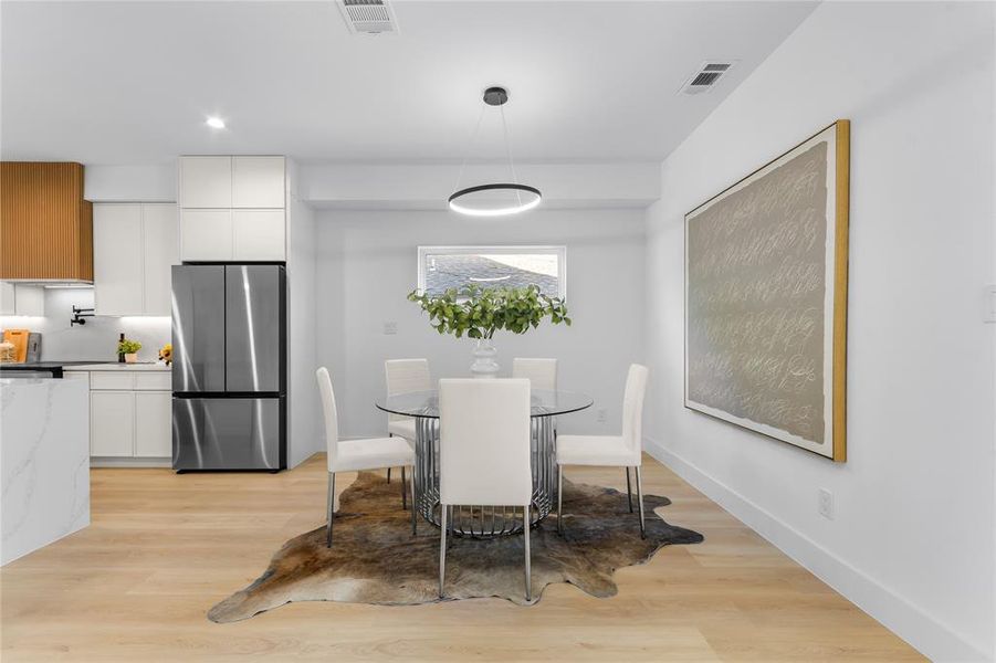 Open-concept living space featuring wood-finish flooring, a contemporary circular chandelier, and a kitchen with two-tone cabinetry and stainless-steel appliances Open-concept living space featuring wood-finish flooring, a contemporary circular chandelier, and a kitchen with two-tone cabinetry and stainless-steel appliances