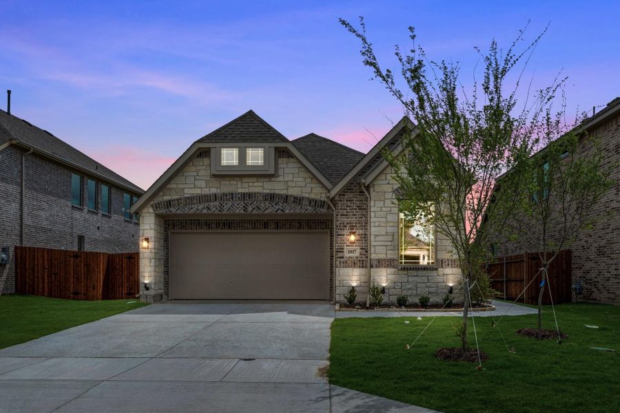 Single-story home with stone and brick exterior, two-car garage, and green front lawn at dusk