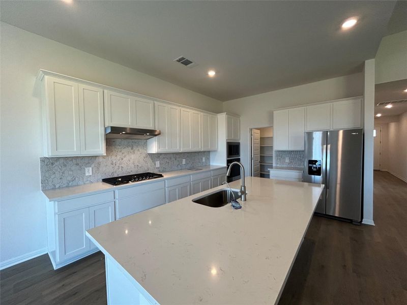 Kitchen featuring white cabinets, stainless steel appliances, decorative backsplash, dark wood-style floors, and light stone counters