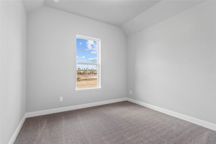 Tucked peacefully in the front of the home is this secondary bedroom featuring neutral toned walls, sloped ceiling, large window, plush carpet flooring, and a walk-in closet.