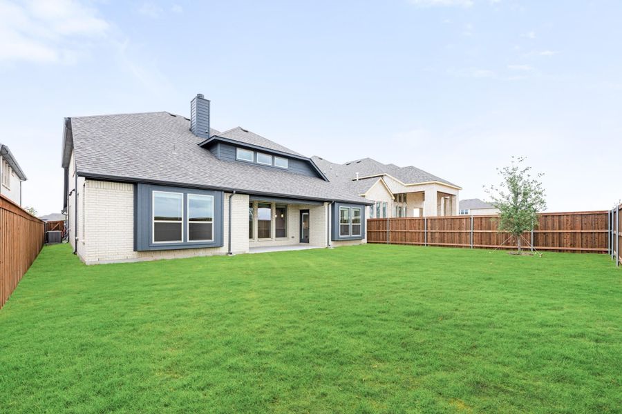Rear view of brick home with gray trim, large fenced backyard, green lawn, and covered patio
