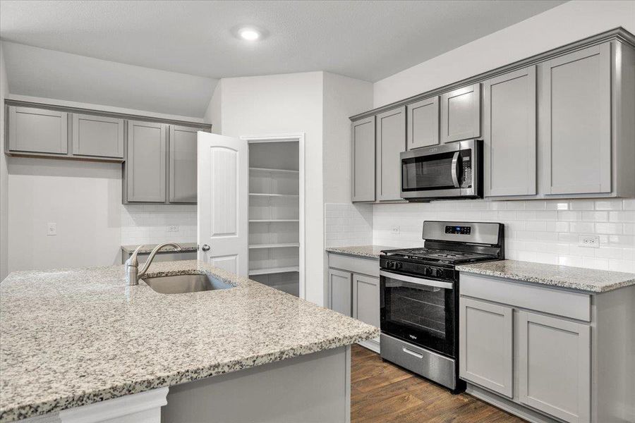The kitchen features granite countertops, gray cabinetry, stainless steel appliances, and a pantry with shelving
