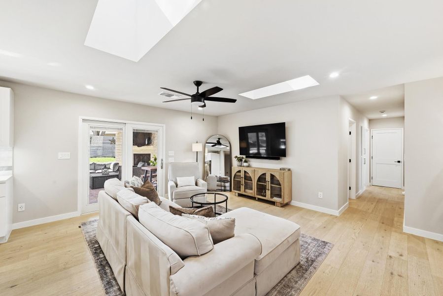 Living room featuring a skylight, light wood-style flooring, a ceiling fan, and recessed lighting