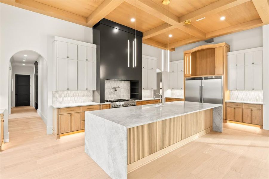 Kitchen featuring arched walkways, white cabinetry, backsplash, light stone counters, and coffered ceiling
