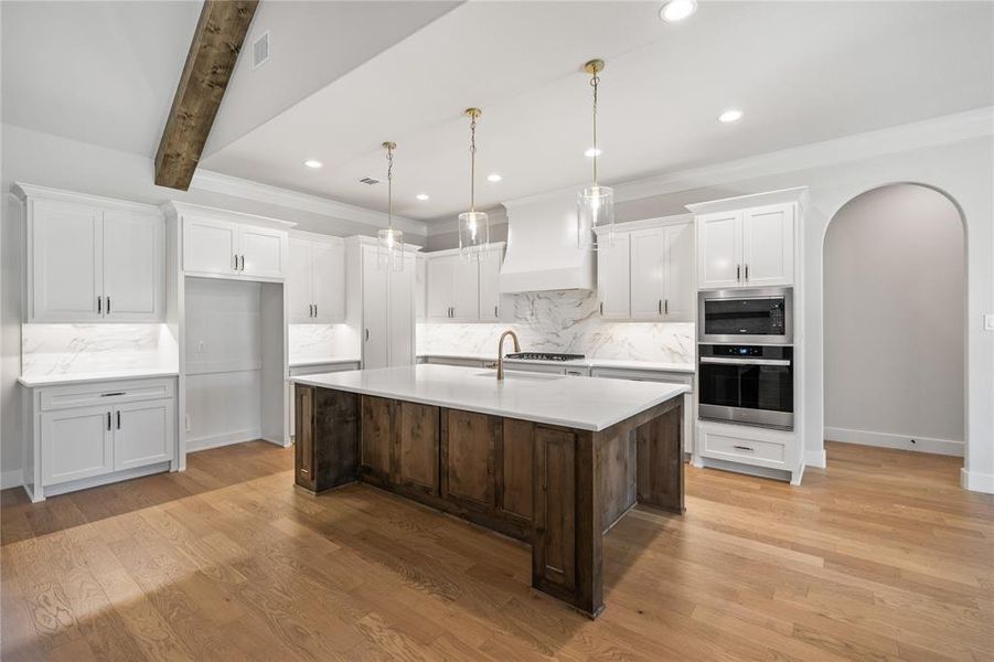 Dual tone kitchen featuring arched walkways, two tone cabinets, stainless steel appliances, light wood finished floors, and an island with sink