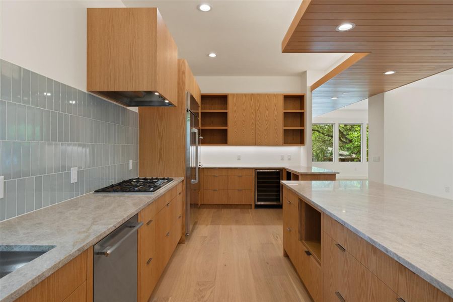 Kitchen featuring light wood-style floors, modern cabinets, recessed lighting, light stone countertops, and backsplash Kitchen featuring light wood-style floors, modern cabinets, recessed lighting, light stone countertops, and backsplash