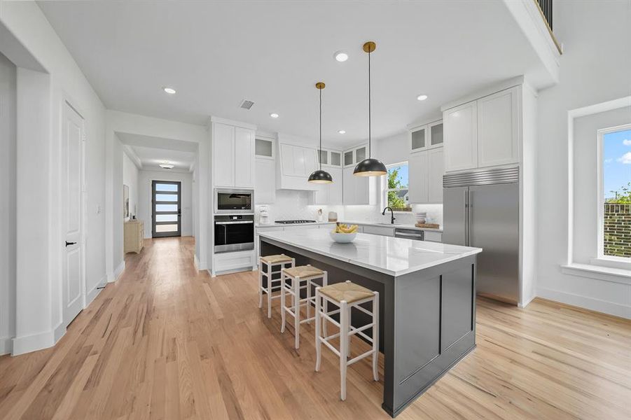 Kitchen featuring glass insert cabinets, white cabinetry, a breakfast bar, decorative light fixtures, and built in appliances