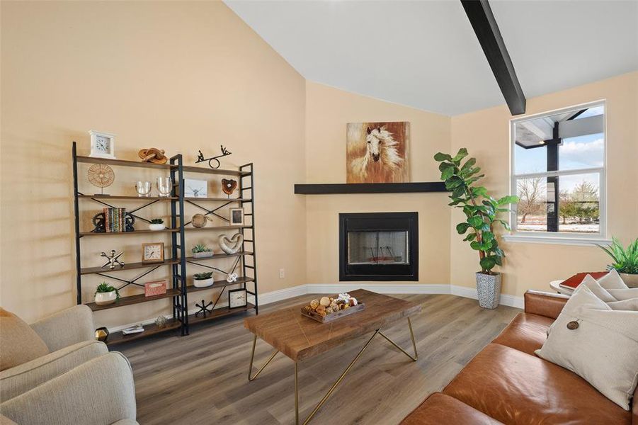 Living area featuring a vaulted ceiling with exposed beam, recessed fireplace with mantle, and wood-finish flooring Living area featuring a vaulted ceiling with exposed beam, recessed fireplace with mantle, and wood-finish flooring