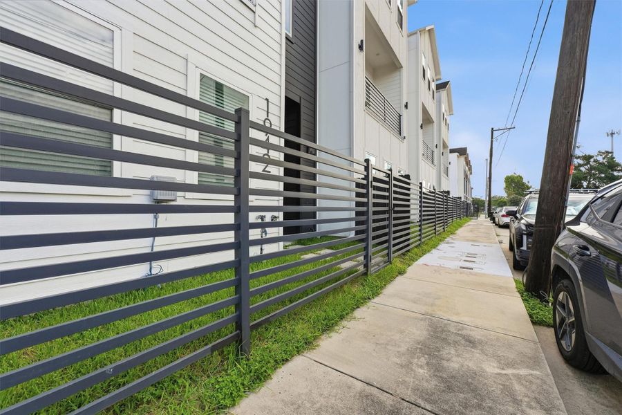 Contemporary townhome exterior featuring a sleek horizontal metal fence, clean modern lines, and a well-maintained sidewalk in a stylish urban streetscape.