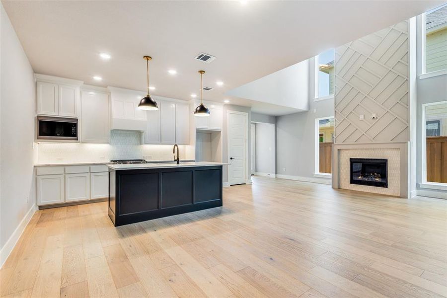 Kitchen featuring a center island with sink, stainless steel microwave, light hardwood / wood-style floors, and white cabinets