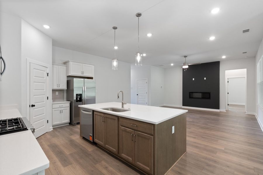 Kitchen island with a stainless steel sink, wood-finish flooring, white cabinetry, integrated stainless steel appliances, and a contemporary linear fireplace