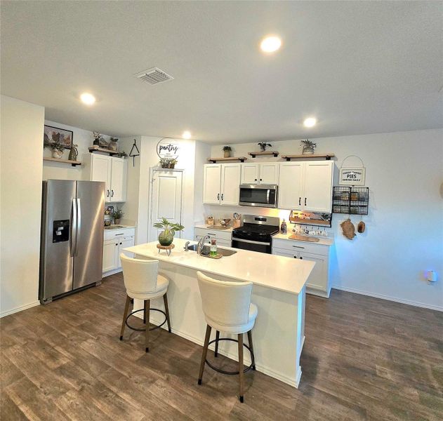 Kitchen featuring a center island with solid surface countertop, wood-finish flooring, white cabinetry, recessed lighting, and stainless steel appliances
