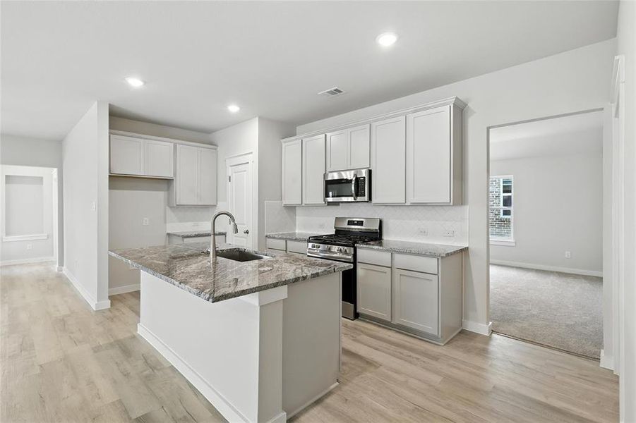 Kitchen with stainless steel appliances, stone countertops, a kitchen island with sink, light wood finished floors, and decorative backsplash