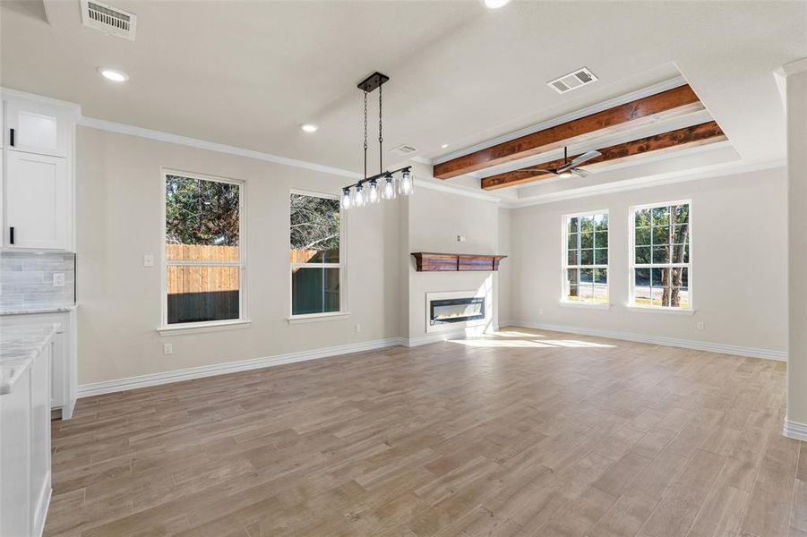 Unfurnished living room with beamed ceiling, light hardwood / wood-style floors, ceiling fan, and ornamental molding