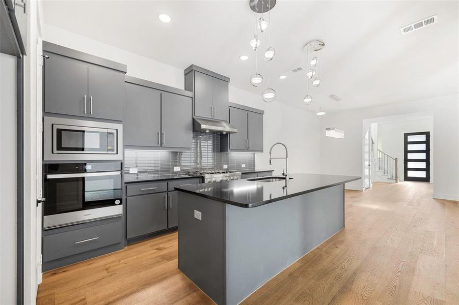 Kitchen featuring oven, under cabinet range hood, a sink, stainless steel microwave, and dark countertops