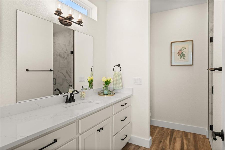 Bathroom vanity featuring a single undermount sink, a stone-finish countertop, and white cabinetry with matte black hardware