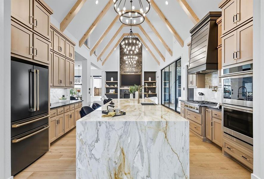 Kitchen with marble backsplash, waterfall marble island, dark quartz counters on either side of the island, beamed ceiling, and stainless steel appliances Kitchen with marble backsplash, waterfall marble island, dark quartz counters on either side of the island, beamed ceiling, and stainless steel appliances