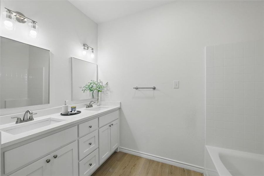 Full bathroom with wood finished floors, double vanity, and baseboards Full bathroom with wood finished floors, double vanity, and baseboards