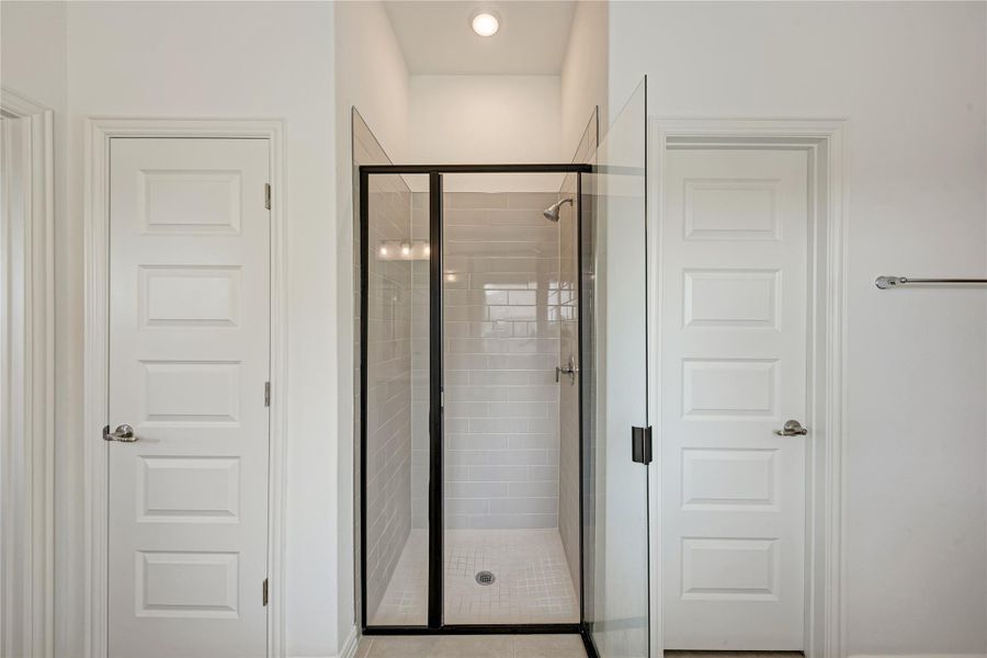 A well-lit shower enclosure with subway tile walls is flanked by two paneled doors, creating a private bath experience.